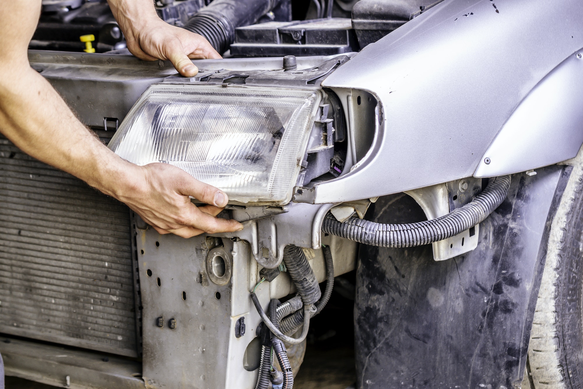 Mechanic repairing the headlight of a car with the gray bodywork.